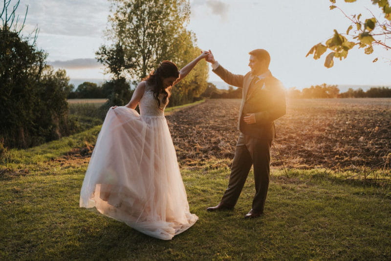 Bride holding out skirt of wedding dress as groom holds her arm in the air - Picture by Grace Elizabeth