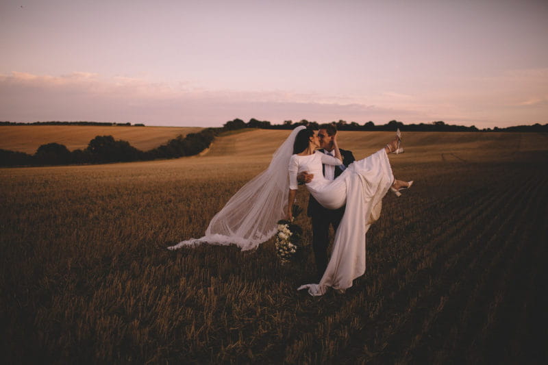 Groom lidting bride up to kiss her in field - Picture by Carrie Lavers Photography