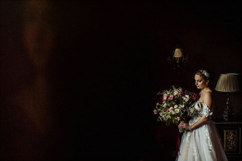 Bride standing holding bouquet in dark room - Picture by Matt Parry Photography