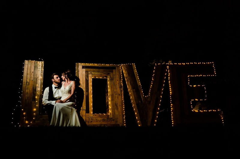 Bride and groom sitting by wooden illuminated LOVE letters - Picture by James Powell Photography