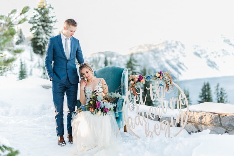 Groom standing next to bride sitting in armchair in snow