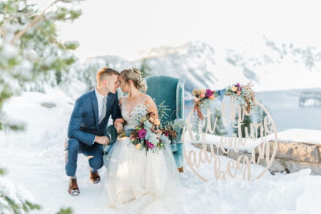 Groom touching heads with bride sitting on chair in the snow