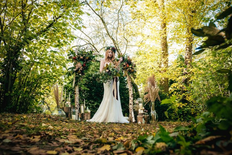 Bride standing in woodland in front of ceremony arch