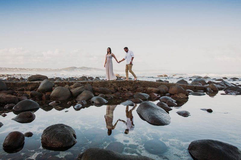 Bride and groom walking holding hands across rockpool - Picture by Estefania Romero Photography