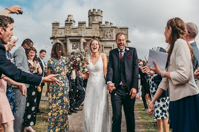 Bride and groom laughing as wedding guests throw confetti over them - Picture by Tracey Warbey Photography