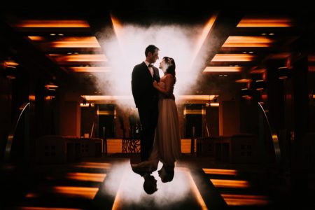 Bride and groom standing in dark orange lit room with smoke behind them - Picture by The Sweet Days