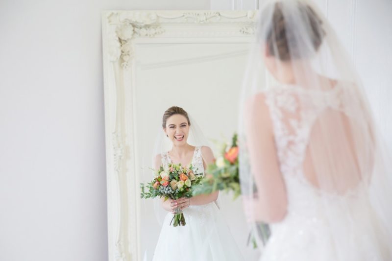 Happy bridre smiling as she looks at her reflection in the mirror - Picture by Helen England Photography