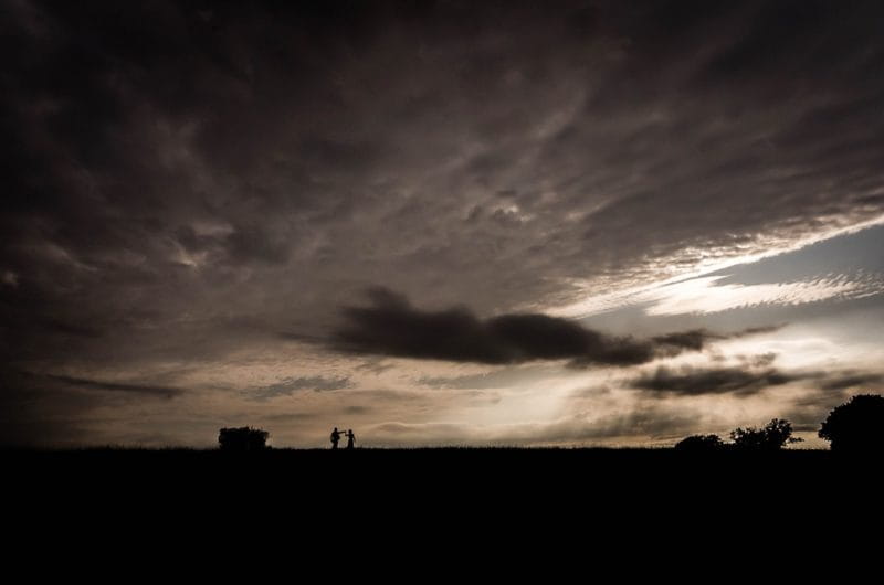 Silhouette of bride and groom in field under dark clouds - Picture by Tammie Louise Photography