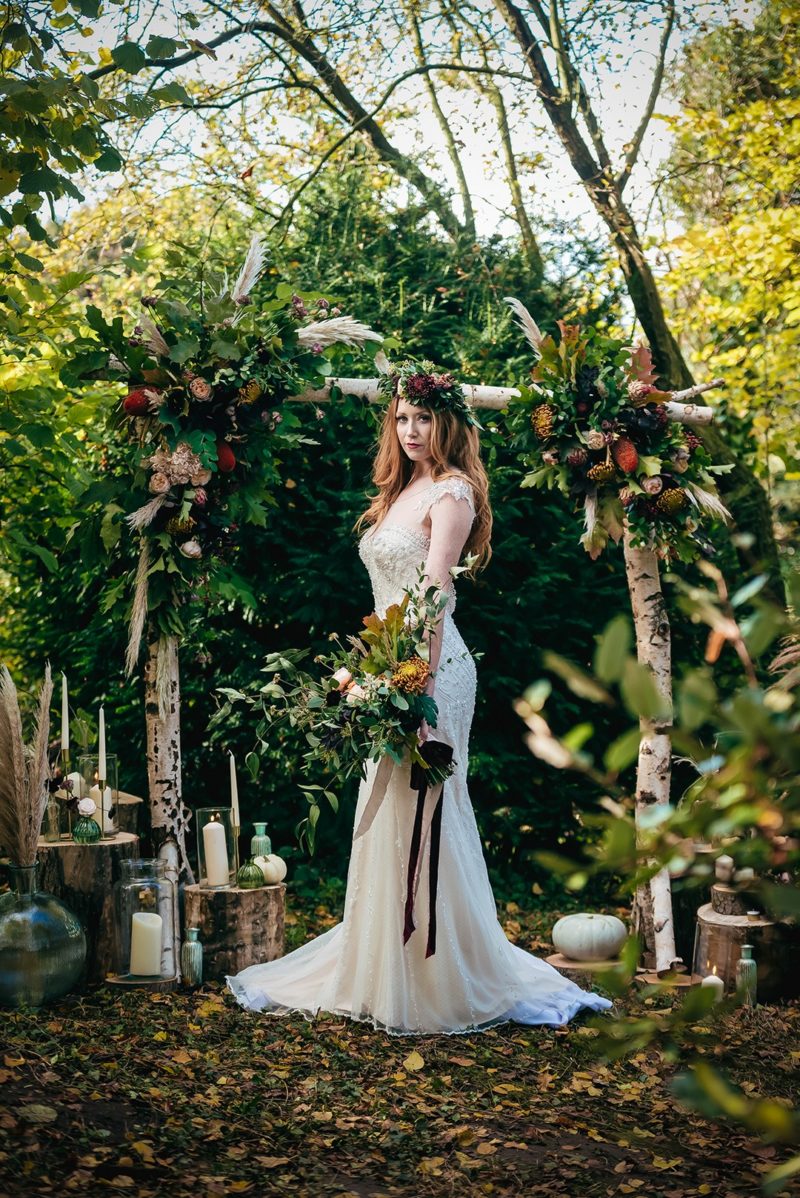 Bride standing in front of ceremony arch in woods