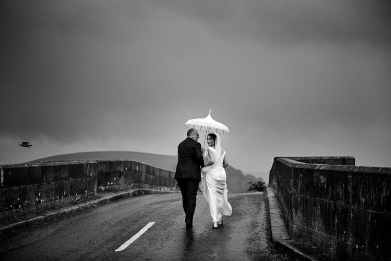 Bride and groom walking over bridge in the rain