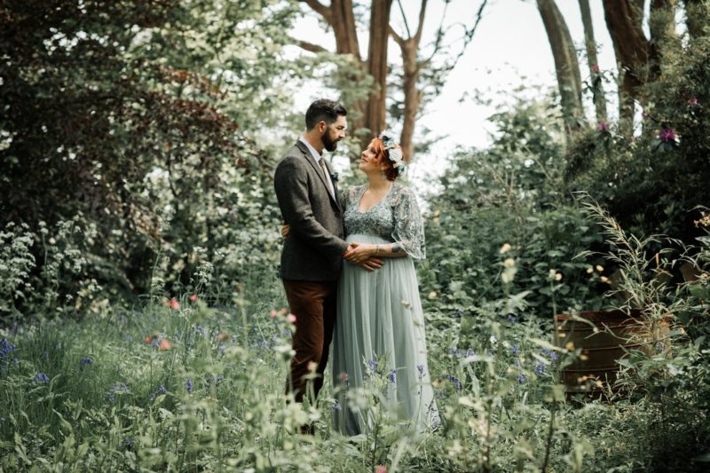 Bride and groom standing amongst greenery in woodland - Picture by Katie Goff Photography