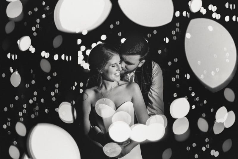 Groom hugging bride from behind surrounded by blobs of light - Picture by Murray Clarke