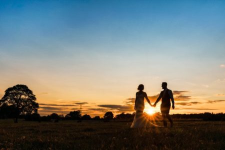 Bride and groom walking holding hands while sun sets between them - Picture by Martin Cheung Photography