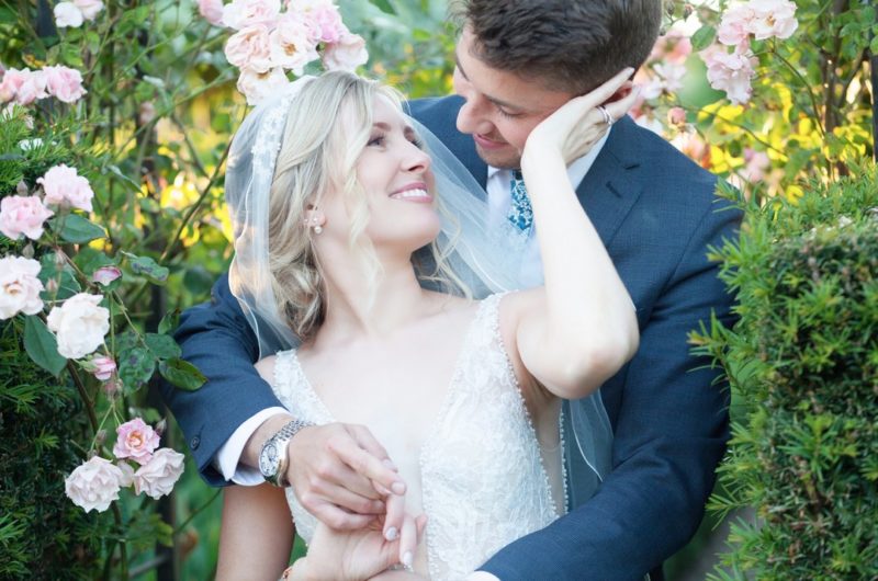 Bride with hand on groom's face as he holds her from behind - Picture by Ella Parkinson Photography