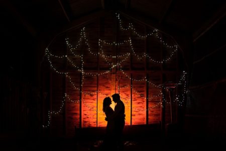 Bride and groom facing each other in the dark with fairy lights behind them - Picture by Penny Young Photography