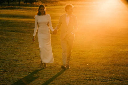 Bride and groom holding hands walking across lawn in hazy sunshine - Picture by Lee Allison Photography