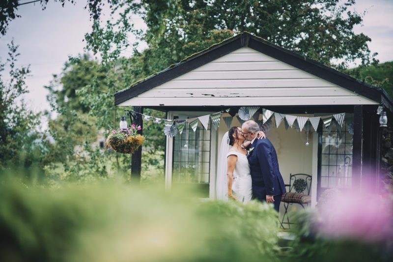 Bride and groom kissing by wooden summerhouse