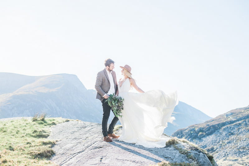 Bride wearing hat with groom on top of mountain - Picture by Laura Jane Photography