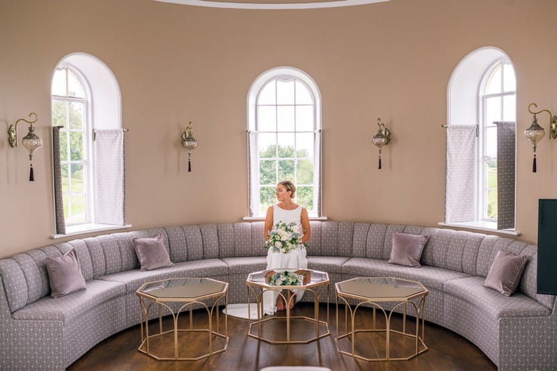 Bride sitting in curved seating area in bedroom at Hawkstone Hall