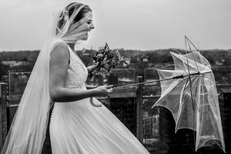 Bride with veil over face laughing at broken umbrella in her hand - Picture by Els Korsten Fotografie