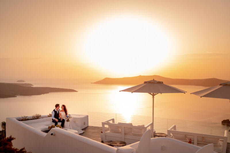 Bride and groom sitting outside venue overlooking sea with big sun in background - Picture by Carpe Diem Photography