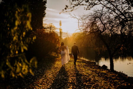 Bride and groom walking down leafy path by water as sun goes down - Picture by Kazooieloki