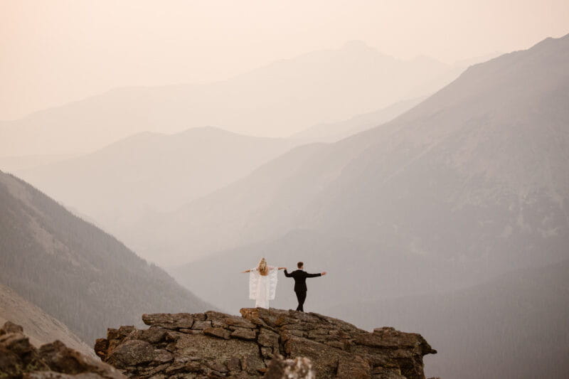 Bride and groom standing on rocks overlooking mountains - Picture by Adventure Instead