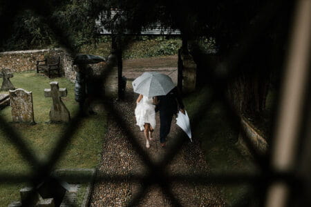 Picture taken through window of bride walking into church under umbrella - Picture by Luke Hayden Photography