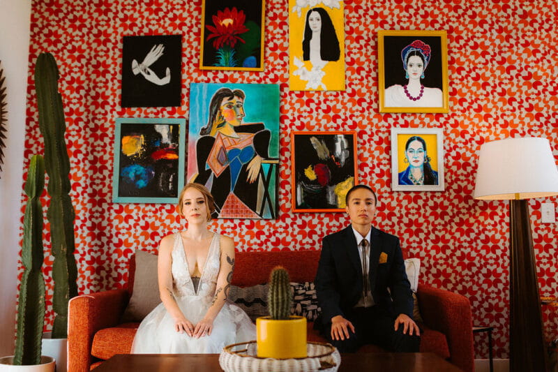 Couple sitting on sofa in front of colourful backdrop of patterned wallpaper and art - Picture by The Hendrys