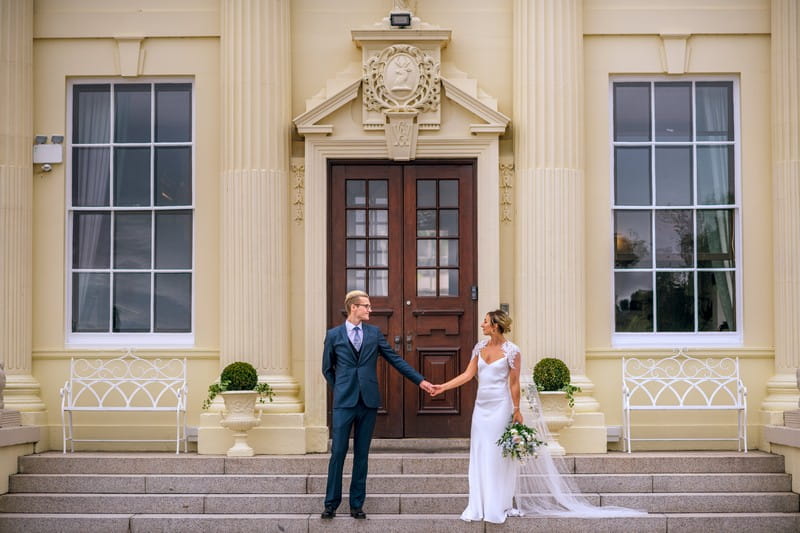 Bride and groom holding hands on steps of Hawkstone Hall