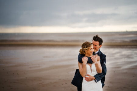 Groom hugging bride from behind on beach - Rob Dodsworth Photography