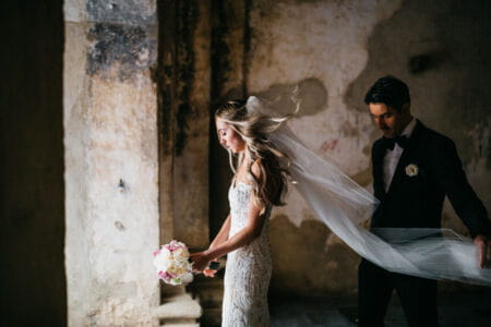 Groom standing behind bride holding end of her veil - Picture by Daniel López Pérez