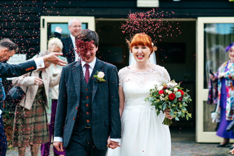 Groom being hit in face with confetti as he walks with bride - Picture by Jordanna Marston Photography