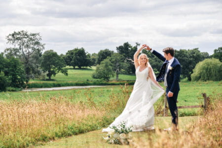 Bride twirling under groom's arm in field - Picture by Memories and Milestones Photography