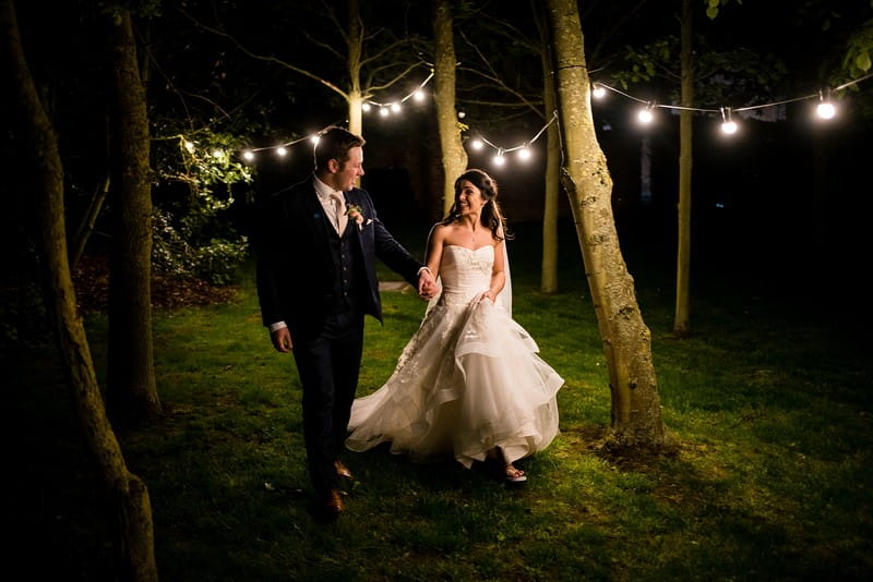 Bride and groom walking past trees at night