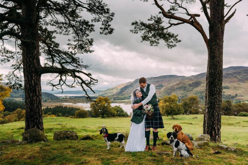 Bride and groom hugging in front of Scottish hills with their dogs - Picture by Eilidh Robertson Photography