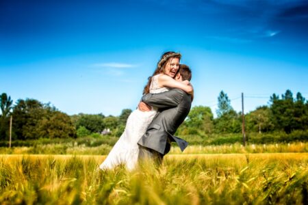 Groom lifting bride up as they hug in a field - Picture by John Young Photography
