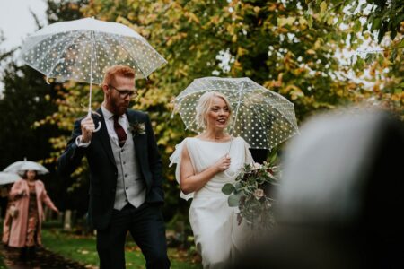 Bride and groom walking with umbrellas - Picture by BGS Weddings