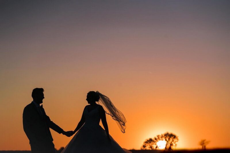 Silhouette of bride and groom against orange sky as sun sets - Picture by Nick Church Photography