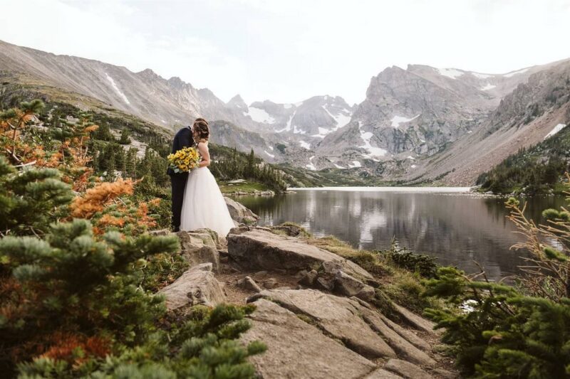 Bride and groom standing by lake with mountains in background - Picture by Larsen Photo Co.