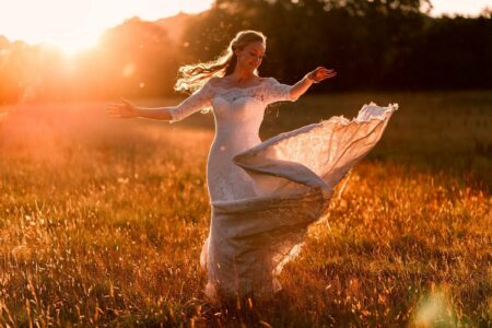 Bride twirling in field in hazy sunshine - Picture by Rich Howman