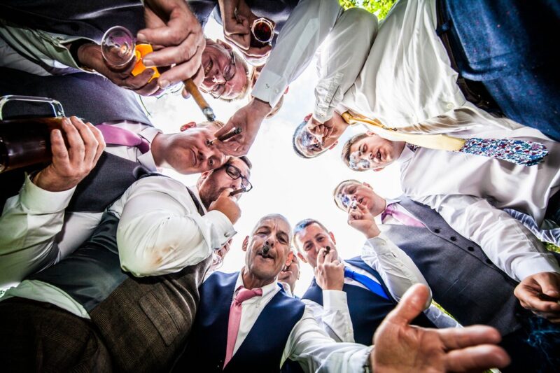 Groomsmen in circle looking down at camera and smoking cigars - Picture by Peter Rollings Photography