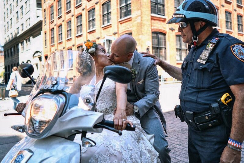 Bride and groom kissing on police officer's scooter as her taps groom on the shoulder - Picture by Emin Kuliyev