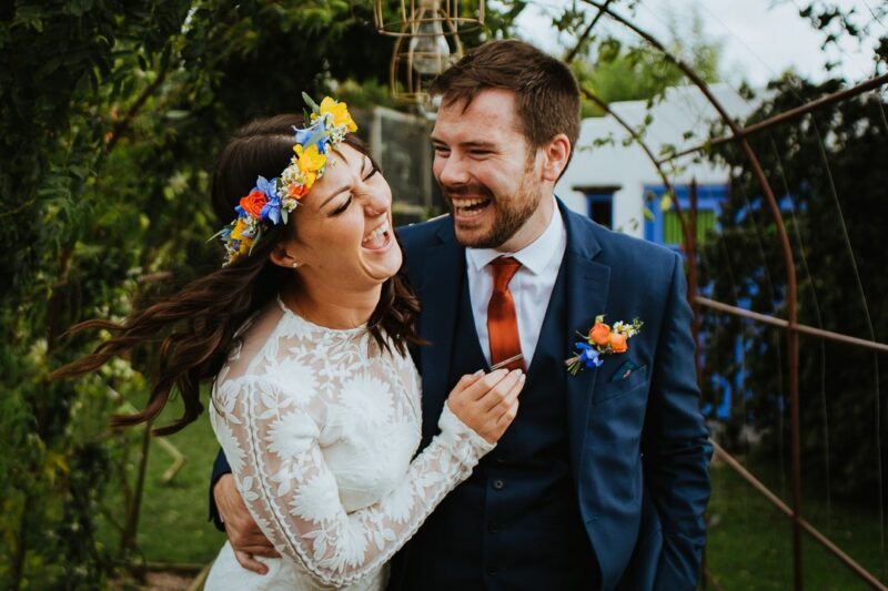 Bride with colourful flower crown laughing with groom - Picture by Alexa Poppe Wedding Photography