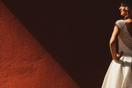 Bride with hands on hips facing red wall - Picture by Aleks Kus