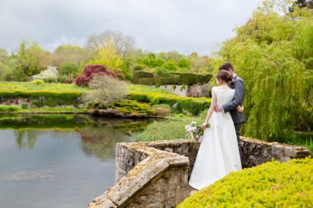 Bride and groom standing by lake at wedding venue - Picture by Helen England Photography