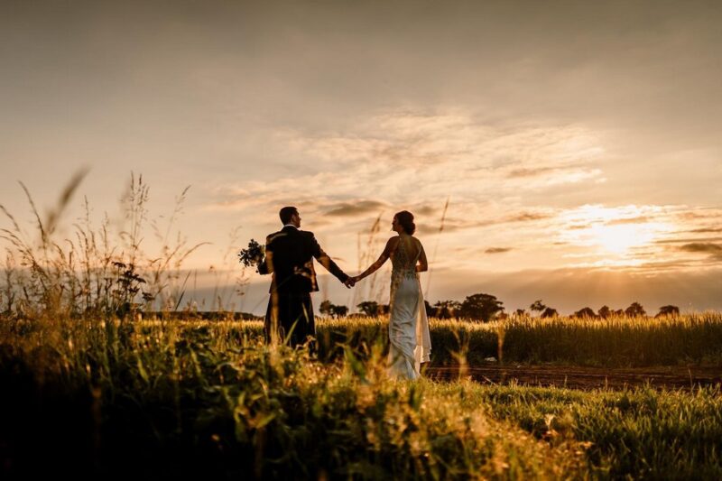 Bride and groom walking holding hands as sun sets - Picture by Hayley Baxter Photography