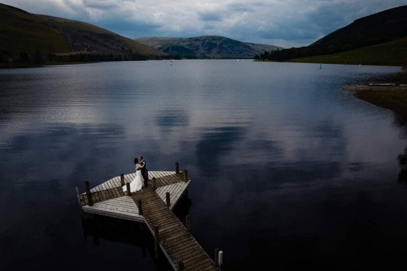 Bride and groom standing on jetty over loch in Scotland - Picture by Andy Dane Photography