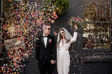 Bride and groom wearing sunglasses smiling as confetti falls around them - Picture by Epic Love Story