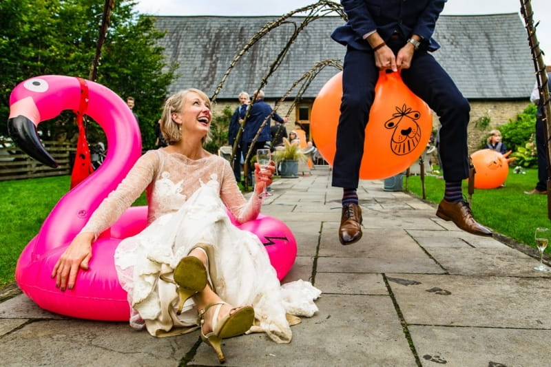 Bride sitting o the ground looking up at man bouncing past on space hopper - Picture by Jonny Barratt Photography